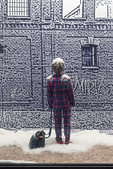 A close up of a small child in pajamas facing a wall in a snowy scene. A small dog in a handbag lies beside the child. The text "MARIA" is visible on the wall.