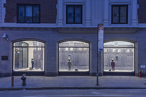 Three window displays seen from the street. Each displays a small child in pajamas facing a wall in a snowy scene alongside a small dog peeking out of a bag.