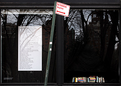 Two outside windows can be seen, one with a large paragraph of printed text, and the other with a small pile of books. A no parking sign can be seen in the foreground.