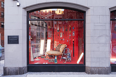 A corner window with various small items hung on a red background. A sign reads "Broadway Windows, New York University."