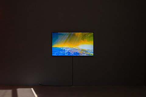 A TV monitor displaying a colorful image hangs in a room with gray walls.