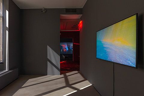 A TV monitor displaying a colorful image hangs in a room with gray walls.