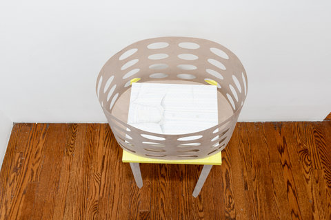Image of an object from the exhibition featuring a table with a beige paper basket on top of it. Inside the basket is a sketch drawing.