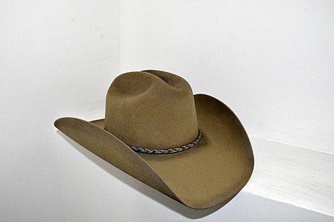 The side view of a light brown cowboy hat. There is a small braided detailing in the center of the hat.