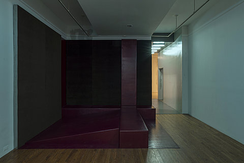 Dark red padded geometric structures sits in the corner of a dimly lit room.