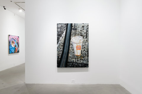 Installation view of one work in the exhibition hanging against a white wall. The image consists of close up composition of a blurry coffee to go cup from Burger King. 