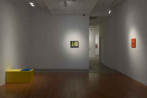 Installation view of several works in the exhibition which is dimly lit. The works shine bright with a white spotlight against the white wall. 