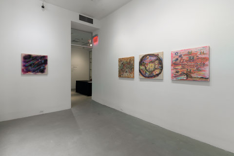 Installation view of two walls in the exhibition. On the right, a dark rectangular painting hangs against a white wall, slightly illuminated by a white spotlight. On the right side wall, there are three pinkish, lighter colored rectangular paintings hanging evenly spaced apart against a white wall.  