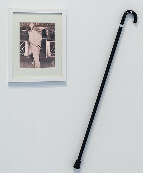 A black cane hangs on the wall next to a framed image of a performer in an all-white tuxedo.