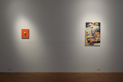 Installation image of two works of art hanging against a white wall. Two spotlights illuminate the works of art. On the left, a small orange painting hangs with a protruding breast-like object. On the right, an abstract mish-mash of real and fake objects crowd the canvas. 