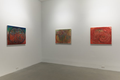 Installation view of three works in the exhibition. The works hang on two walls, that converge at a corner. Each work is evenly spaced out and slightly illuminated by a white spotlight. The white walls are contrasted by a cement floor in the foreground. 