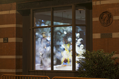 Shot from outside of a red brick building, a large projection can be seen on the wall through the window.