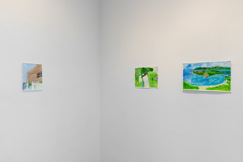 Installation view of three drawings in the exhibition on two walls. On the left wall, there is a drawing of a brown house. In the foreground is a white picket fence and grass with a blue sky in the background. In the middle, on the right side wall, is a drawing of what looks like a figure underneath a white blanket on a green grassy plain. A sun and sky hang in the right upper corner of the drawing. On the right most image, there is a landscape drawing of green hill islands and blue water with yellow sand beaches. 