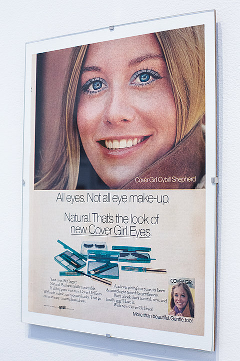 A framed print of a makeup advertisement showing a woman's face wearing blue eyeshadow.