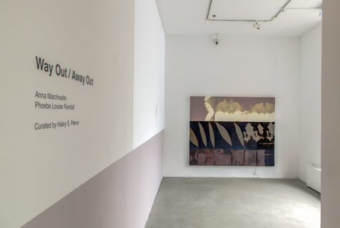 Installation image of the exhibition featuring a side view of wall text on the left wall and a painting hanging on the back wall. The wall text, skewed from camera angle states, "WAY OUT/AWAY OUT. ANNA MARCHISELLO AND PHOEBE LOUISE RANDALL. CURATED BY HALEY S. PIERCE."