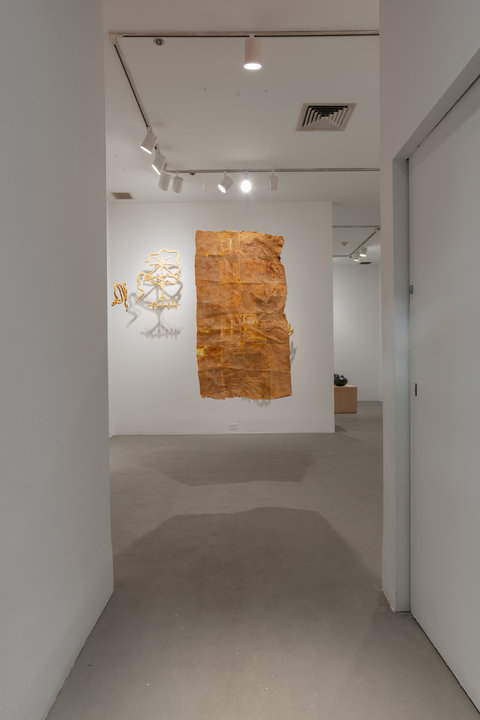 Image featuring the hallway leading into an exhibition room featuring a large rectangle of wrinkled paper mache or cardboard hanging from the ceiling. 