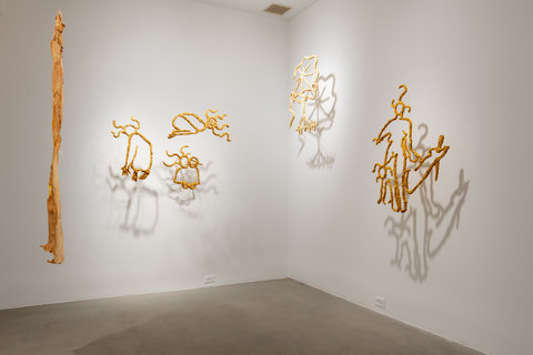 Installation view of various hanging paper mache abstract shapes twisting and turning together. The structures are hanging from the wall, just off the wall, so the light reflects their shadows onto the wall. 