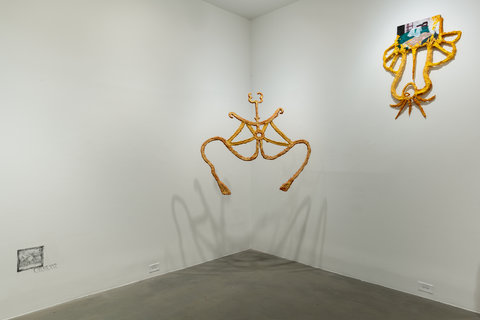 Installation image of three works in the exhibition. On the left wall, near the bottom, a small square is sketched directly onto the wall. In the middle, where two walls converge into a corner, an abstract sculpture of paper mache hangs just in front of the wall, the shadow reflecting onto the corner behind it. On the right wall, above, another abstract paper mache sculpture is mounted to the wall. 