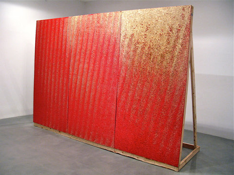Gallery installation view that shows a very large, three red panels. The panels are held up by wood stilts. 