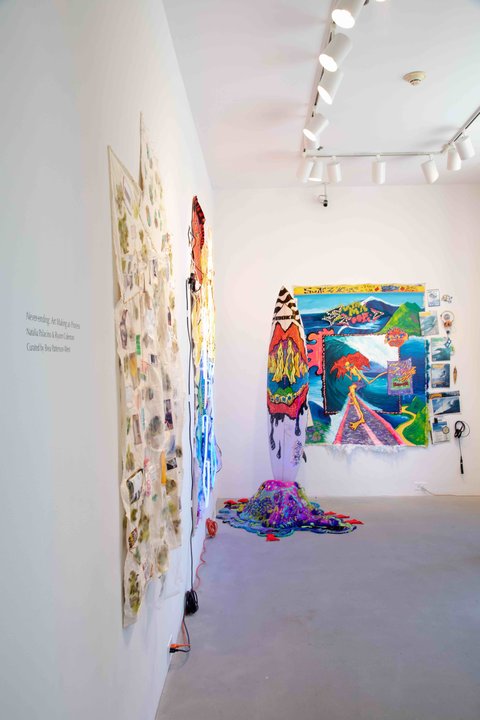 Installation image taken from the entrance of the gallery. On the left side wall, at an angle are two works hung up side by side, the frontal view is obstructed from thsi camera angle. On the back wall, a colorful, abstract painting hangs with various blocks of color. 