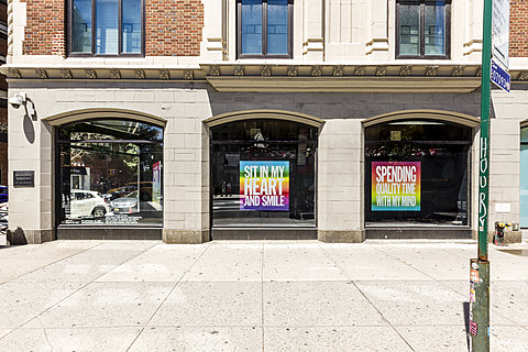 Two windows displays have hanging prints of white text over a multicolor gradient background. One reads, "Sit in my heart and smile," and the other, "Spending quality time with my mind."