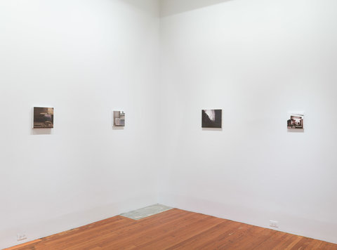 Installation view of four paintings on two walls that converge at the corner. The images are evenly spaced apart on the bright white wall. 