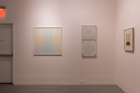 Installation image of three paintings. On the left wall, which is angled facing the camera head on, consists of two paintings. The painting on the left wall consists of six overlapping squares in different muted, pastels of blue, green orange, yellow, and purple. The painting on the right features two black and white sketches, one hung above the other. The sketches consist of mandala-like drawings.  