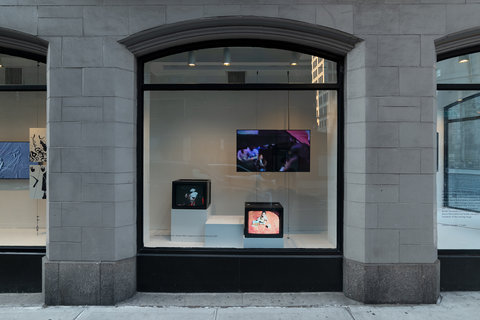 Installation view featuring three monitors in the window, staggered in size. On the bottom, a small monitor, a bit higher up on the left, is a similarly sized monitor. In the back on the right, higher up, is a larger flat screen monitor.  