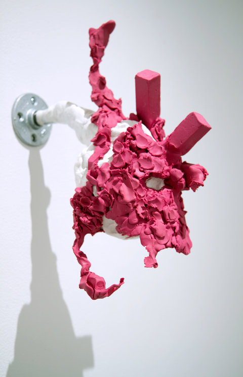 Installation image of a work in the exhibition that features a white branch protruding from a silver, metal disc. The white turns into a deep fuschia pink color and is molded into several pinched, clay branch like arms. 