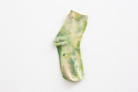 Image from the installation featuring a green and white sock hanging on a wall. 