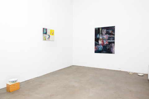 Installation view of the exhibition featuring three pieces of art work. On the left most side of the image, on the ground, sits an orange-ish wooden block. On top the block, sits a blue China bowl with blue liquid inside. On the left wall, a painting hangs with six abstract sections in an organization of three by two. The panels are illegible from camera view. On the right side wall, a drawing of a figure is painting with abstract, dark colors. The figure holds a gun, and points it towards the viewer with their right hand, while holding a gun to their own head with their left hand. The figure looks out into the viewers eyes. 