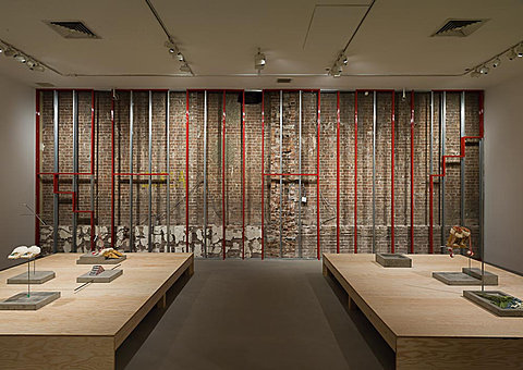 In a gallery, red posts on the back wall spell out "REMAIN."