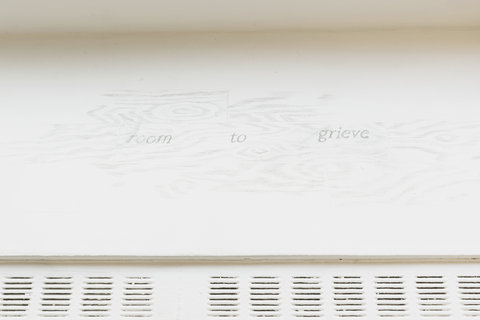 Close-up image of writing on the bench in the exhibition room. Sketched in pencil, the writing states, "ROOM TO GRIEVE." 