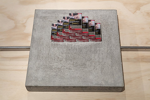 A stacked pile of cigarette packs sit on a concrete plinth.