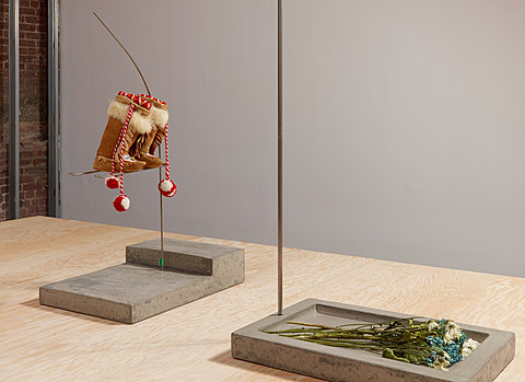 A pair of moccasins hang next to flowers lying on a concrete plinth.