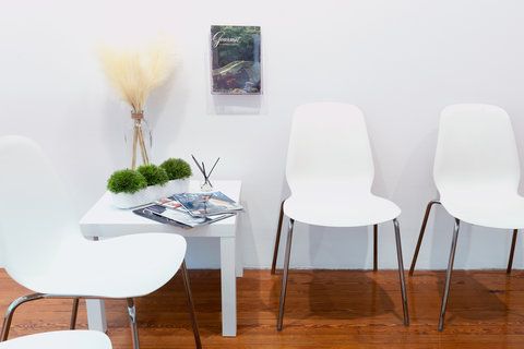 Close-up view of a section of the installation featuring four white chairs, a side table with plants and magazines, and an image on the wall. 