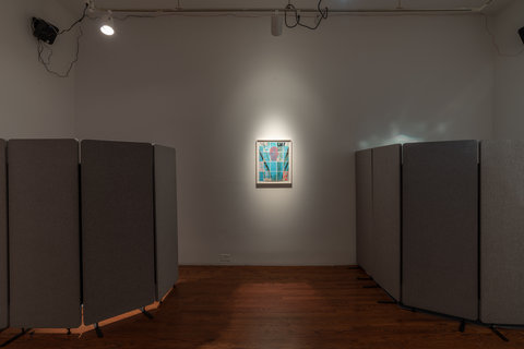 Installation view of the exhibition featuring a dark, unlit room with a spotlight pointing at a piece in the center. On either side of the painting, are grey fabric room dividers.  