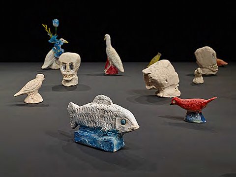A detail of some small ceramic sculptures showing skulls, fish, and birds on a black surface.