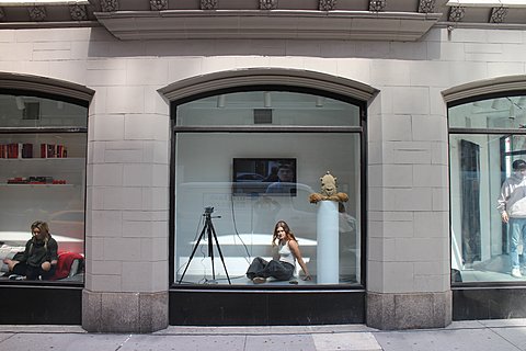 A person sits in a small display next to a tripod, a plinth, and a television.