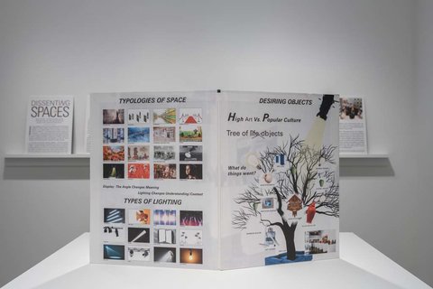 Image of a pamphlet on a white pedestal. The pamphlet features to page, on the left, a collection of smaller images, on the right, there is a sketch tree with some writing, though it is illegible from image quality. 