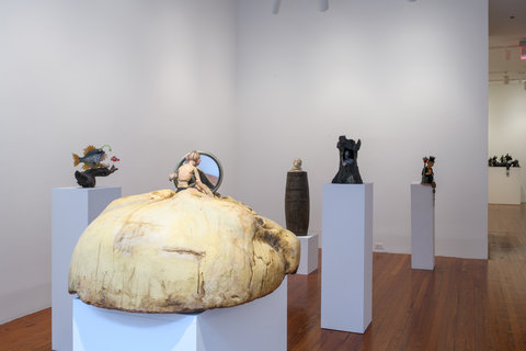 Installation view of six pedestals in the exhibition. Sculptures sit atop the pedestals and are scattered across the room. 
