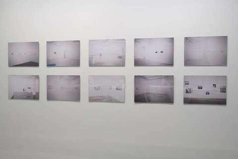 Installation image of ten black and white rectangular photographs in two rows of five hung on a white wall. From the camera angle, they seem to be several landscapes. 
