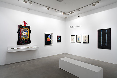 Several framed artworks hang on a gallery's walls. Text on one wall reads "Spells."