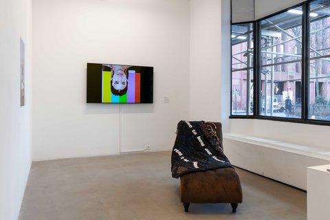 Installation view of the entire exhibition room include two walls, four window panes that look out onto the street, a sculpture in the center of the room, a video monitor, and a photography print.