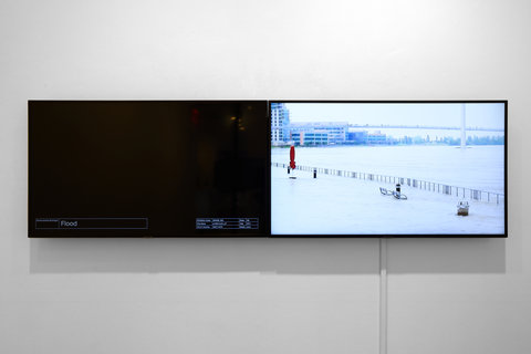 Installation view of the exhibition featuring two television monitors mounted to a white wall. On the left, a blank screen monitor is black. On the right, the monitor shows a still from the video compilation of a snowy landscape. 