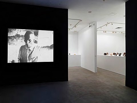 A black-and-white projection of a figure is projected on a black wall. In the background is a room with white walls and multiple sculptures.