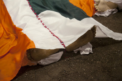 Close-up view of the installation featuring, orange and white and green fabric, part of the flags of India and Pakistan covering a fake body. In this, the feet of the body are emerging from the bottom of the flag. 