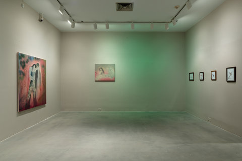 Installation view of several paintings in the exhibition. There is one large painting on the left wall. On the back wall, there is one painting and the wall is half washed with green light. On the right, four framed works of art are mounted on the wall. The walls are painted grey. 