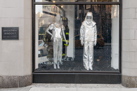 Image of two mannequins in the exhibition. The left mannequin wears a silver shirt and silver pants. The mannequin on the right wears a full silver space-like costume with a silver fabric helmet. 