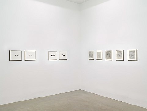 Two rows of framed drawings hang on perpendicular walls of a gallery.